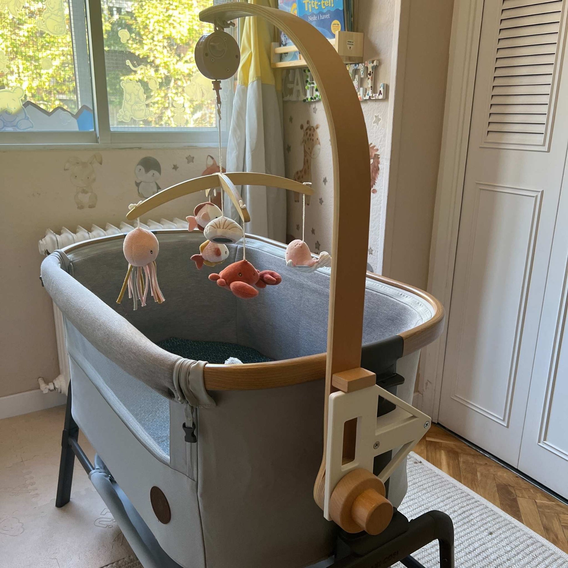 Maxi-cosi_Iora white CribClamp attached to the bedside crib with a little dutch musical mobile. View of the Maxi-cosi co-sleeper and baby mobile attachment adapter bracket from the head side of the bedside cot